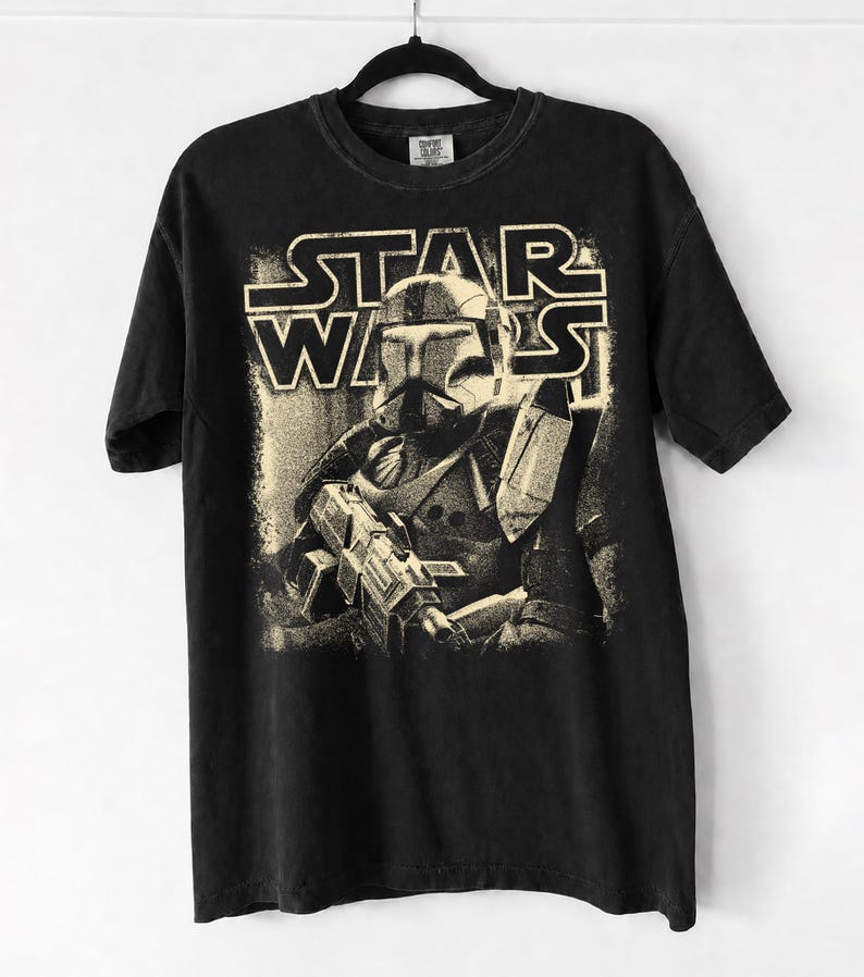 Peut inclure: Un t-shirt noir &agrave; manches courtes avec une impression graphique couleur cr&egrave;me repr&eacute;sentant un clone trooper Star Wars tenant un fusil blaster. Le texte STAR WARS est imprim&eacute; dans une police grasse et stylis&eacute;e au-dessus du personnage.