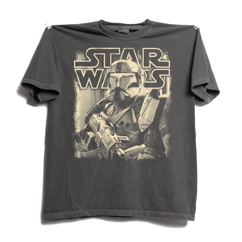Peut inclure: Un t-shirt gris anthracite &agrave; manches courtes avec une impression graphique couleur cr&egrave;me repr&eacute;sentant un clone trooper Star Wars portant un casque et tenant un fusil blaster. Le texte STAR WARS est imprim&eacute; en gras au-dessus du personnage.