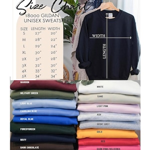 May include: A navy blue unisex sweatshirt hangs on a wooden hanger, with a size chart and color options displayed. The size chart shows measurements in inches for sizes S to 5X. Below are stacks of folded sweatshirts in various colors.
