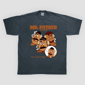 May include: Dark gray t-shirt featuring a graphic of Mr. Potato Head characters. The design includes the text "MR. POTATO HEAD" in brown lettering, along with the phrase "Hey, watch it, buddy!"