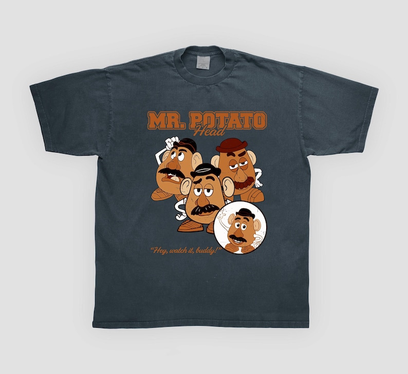 May include: Dark gray t-shirt featuring a graphic of Mr. Potato Head characters. The design includes the text "MR. POTATO HEAD" in brown lettering, along with the phrase "Hey, watch it, buddy!"