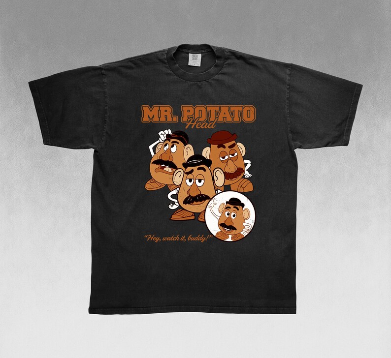 May include: Black t-shirt featuring a graphic of Mr. Potato Head with the text "MR. POTATO HEAD" in brown. The design includes multiple Mr. Potato Head characters and the phrase "Hey, watch it, buddy!"