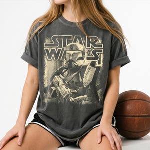 Peut inclure: Un t-shirt gris anthracite &agrave; manches courtes avec un graphisme vieilli de couleur cr&egrave;me repr&eacute;sentant un clone trooper Star Wars tenant un fusil blaster. Le texte STAR WARS est imprim&eacute; dans une police audacieuse au-dessus de l'illustration.