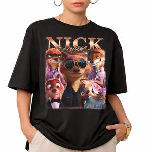 May include: Black t-shirt featuring a graphic of Nick Wilde from Zootopia. The design includes multiple images of the character, with the name "NICK Wilde" in gold lettering across the top. The shirt is a casual, unisex style.