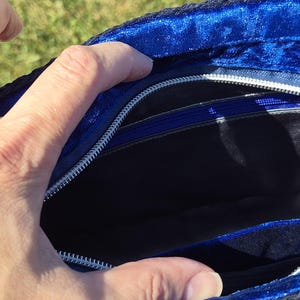 May include: A royal blue velvet handbag interior featuring a black fabric lining, a silver-toned metal zipper closure along the top edge, and an additional internal zippered pocket with a blue pull tab for secure storage of small items.