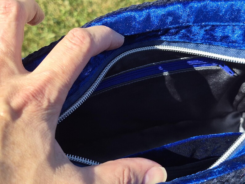May include: A royal blue velvet handbag interior featuring a black fabric lining, a silver-toned metal zipper closure along the top edge, and an additional internal zippered pocket with a blue pull tab for secure storage of small items.