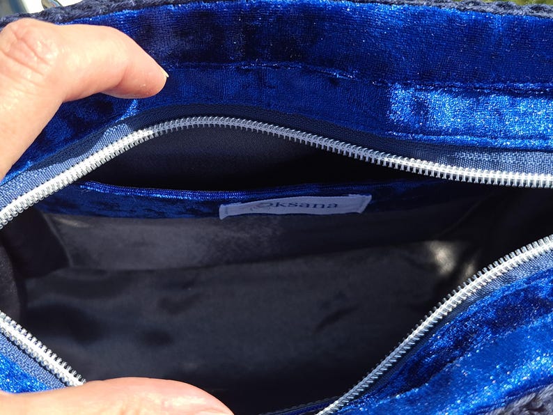 May include: A deep blue velvet bag interior featuring a silver zipper closure along the top edge. The inside is lined with a dark fabric and includes a small white rectangular label with the text Oksana stitched onto the inner pocket area.
