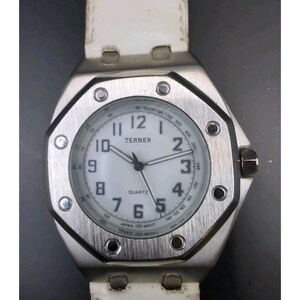 Puede incluir: Un reloj plateado con esfera blanca y correa de cuero blanca. La esfera muestra la marca "TERNER" y la palabra "QUARTZ". El reloj tiene una escala taquimétrica y un movimiento japonés.