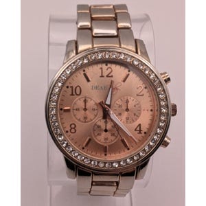 May include: A rose gold wristwatch with a silver band. The watch face has a rose gold hue with the word "DEAR" printed on it. The bezel is encrusted with small, clear crystals. The watch has three smaller dials and a date display.