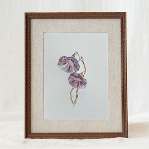 May include: A framed watercolor painting featuring two purple morning glory flowers on a light background. The artwork is encased in a textured beige mat and a dark brown wooden frame with a decorative edge, showcasing a delicate floral illustration.