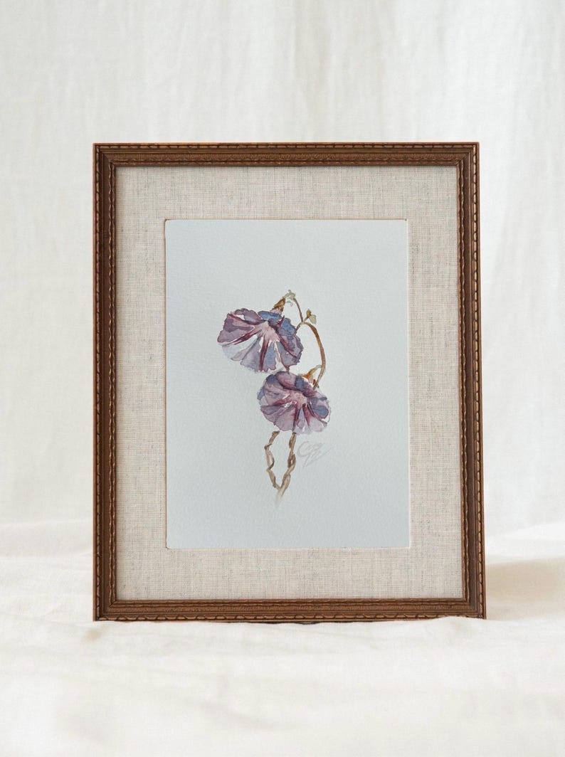 May include: A framed watercolor painting featuring two purple morning glory flowers on a light background. The artwork is encased in a textured beige mat and a dark brown wooden frame with a decorative edge, showcasing a delicate floral illustration.