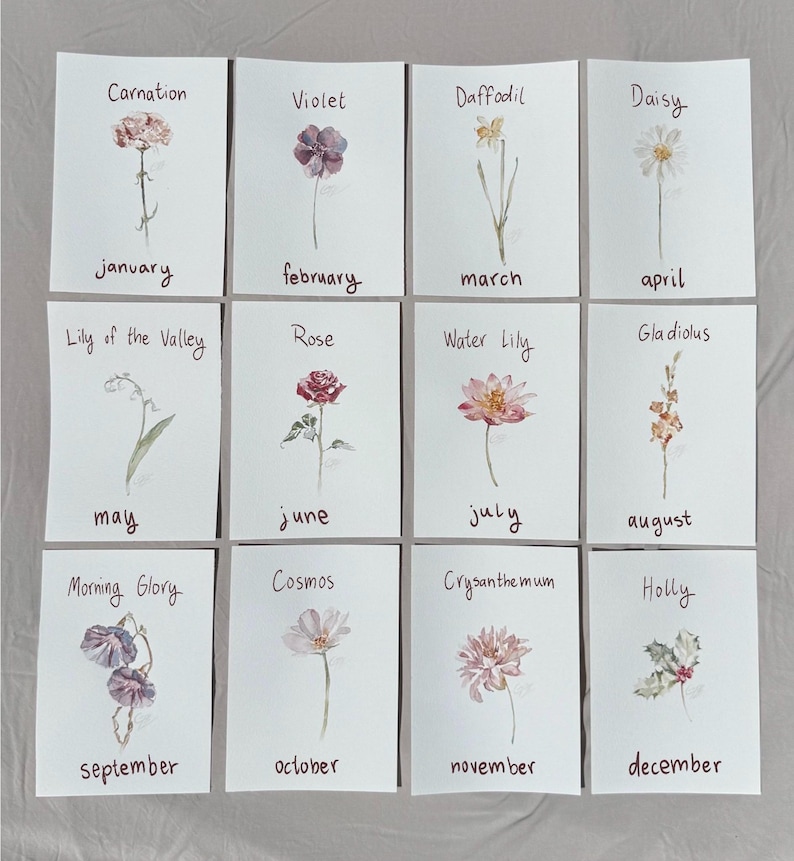 May include: A set of twelve rectangular cards featuring watercolor illustrations of birth month flowers. Each card displays a flower name and the corresponding month in handwritten text, including Carnation, Violet, Daffodil, Daisy, Lily of the Valley, Rose, Water Lily, Gladiolus, Morning Glory, Cosmos, Chrysanthemum, and Holly.