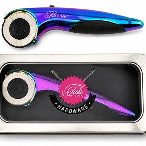 May include: A rainbow iridescent rotary cutter with a circular blade and black handle. The cutter is shown separately and inside a metal tin with the text "Tula Pink HARDWARE".