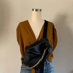 May include: A black leather fanny pack with a gold chain strap worn over a brown blouse and blue denim skirt.