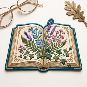 May include: An embroidered patch shaped like an open book with a teal border. The pages feature detailed stitching of blue forget-me-nots, purple lavender, pink flowers, green ferns, and ivy leaves. Gold filigree accents decorate the corners.