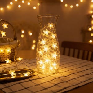 May include: A clear glass vase filled with warm white star-shaped fairy lights. The vase sits on a checkered tablecloth, with additional star lights in the background, creating a cozy, illuminated ambiance. Decorative lighting.