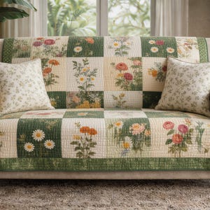 May include: A floral-patterned sofa with two matching throw pillows. The sofa has a quilted cover with a patchwork design featuring various flowers in shades of pink, orange, and white against a green and cream background. The pillows have a similar floral pattern.