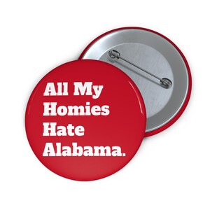 May include: A red button with the text "All My Homies Hate Alabama" in white. The button has a metal pin back. The button is round and has a shiny finish.