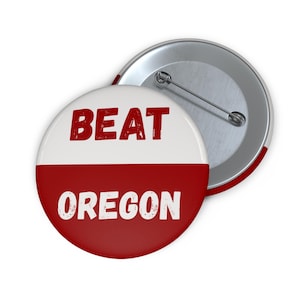 May include: A round button with the words "BEAT OREGON" in white text on a red and white background. The button has a metal pin on the back and a red edge.