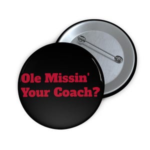 May include: A black button with the text "Ole Missin' Your Coach?" in red. The button has a pin back and a silver metal backing. The button is a round shape.