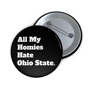May include: A black button with the text "All My Homies Hate Ohio State" in white. The button is round and has a pin on the back. The button is a novelty item.