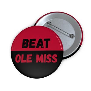 May include: A round button with a red and black design. The top half is red with the word "BEAT" in black. The bottom half is black with the words "OLE MISS" in red. A second button is visible.