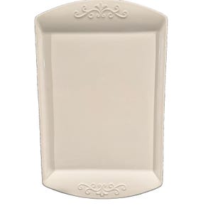 May include: A rectangular off-white ceramic serving tray with a smooth, glossy finish. The tray features a raised, symmetrical scrollwork design embossed on both the top and bottom edges, providing a decorative border to the flat center surface.