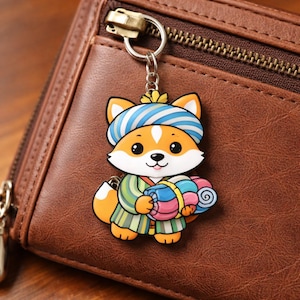 May include: A colorful fox keychain with a blue and white striped hat and a green and yellow outfit. The fox is holding a bundle of rolled-up blankets. The keychain is attached to a brown leather wallet.