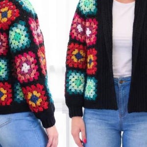 Könnte beinhalten: Eine schwarze Häkeljacke mit bunten quadratischen Mustern. Die Quadrate weisen rote, blaue, gelbe, grüne und weiße Designs auf. Die Jacke wird über einem weißen Oberteil und einer blauen Jeans getragen.