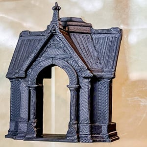 May include: A dark gray, three-dimensional printed architectural model of a gothic archway. The structure features a pointed roof, vertical columns flanking the central opening, and intricate linear textures across the surface of the facade.
