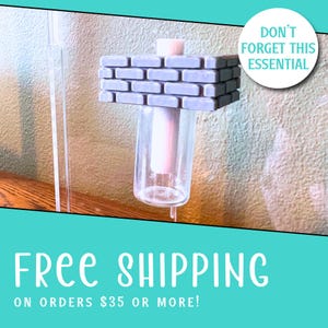 May include: A clear glass cylindrical container topped with a rectangular, light purple, brick-patterned block. The object features a central vertical pillar extending through the center of the brick structure into the glass vessel below.