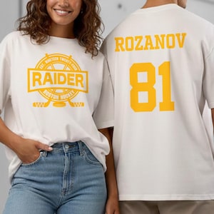 Könnte beinhalten: Zwei Personen tragen weiße T-Shirts mit gelben Grafiken. Die Grafik auf der Vorderseite des Shirts lautet "RAIDER BOSTON HOCKEY" mit gekreuzten Hockeyschlägern. Auf der Rückseite des Shirts stehen der Name "ROZANOV" und die Nummer "81".