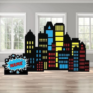 May include: A black cityscape silhouette with colorful windows in blue, yellow, and red. A comic book style speech bubble with the word "NAME" is on the left. The cityscape is a decorative item.
