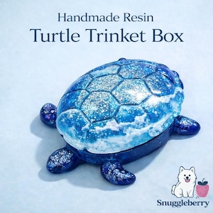Könnte beinhalten: Handgefertigte Schildkröten-Schmuckschatulle aus Harz in Blautönen. Der Deckel hat ein strukturiertes, ozeanähnliches Design mit weißen Akzenten. Die Box ist schildkrötenförmig, mit vier dunkelblauen Füßen. Der Text "Handmade Resin Turtle Trinket Box" ist oben zu sehen.