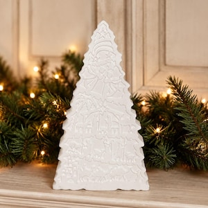 May include: A white, triangular, tree-shaped decorative object featuring an embossed nativity scene. The design includes carved figures of people, animals, and a star at the top, all rendered in a matte white finish with a flat base for stability.