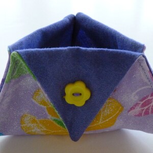 May include: A handmade fabric container with a triangular shape. The exterior features a lavender floral pattern with yellow and pink accents, while the interior and top flaps are a solid blue. A yellow flower-shaped button secures the flap.