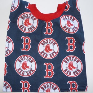 May include: A navy blue bib with a red trim and a repeating pattern of the Boston Red Sox logo. The logo features a red baseball with white stitching, a red 'B' and the words 'Boston Red Sox' in white.