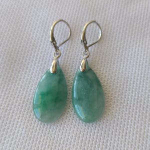 Peut inclure: Une paire de boucles d'oreilles en jade en forme de goutte. Les boucles d'oreilles sont dotées de fermoirs à levier argentés et de pierres de jade en forme de goutte. Le jade est vert clair translucide avec des veines vertes plus foncées.