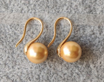 May include: A pair of gold-tone earrings with a single, large, golden pearl on each earring.