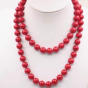 May include: A double-strand necklace featuring large, round, bright red beads. The beads are evenly spaced and strung together, creating a bold and classic jewelry piece. The necklace is displayed on a white mannequin bust.