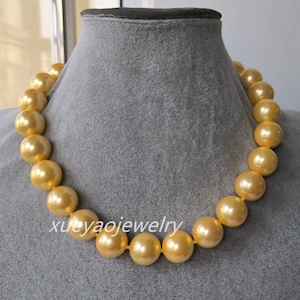 May include: A golden-yellow pearl necklace displayed on a grey mannequin. The necklace features large, round pearls strung together. The text "xuyaojewelry" is visible on the necklace. The pearls have a lustrous sheen.