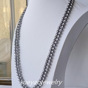 Puede incluir: Un collar de perlas de doble cadena hecho de perlas grises. El collar se muestra en un maniquí blanco.