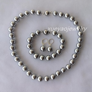 Puede incluir: Un conjunto de collar, pulsera y pendientes de perlas plateadas. El collar y la pulsera están hechos de perlas grandes y redondas. Los pendientes son pequeños y redondos.