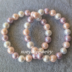 Op de afbeelding: Twee parel armbanden met witte, roze en lavendel parels. De armbanden zijn gemaakt van ronde parels en zijn aan elkaar geknoopt.