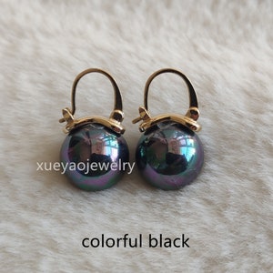 Op de afbeelding: Een paar gouden oorringen met een zwarte parel hanger. De parels hebben een iriserende glans met hints van groen en paars.