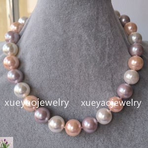Puede incluir: Un collar de perlas multicolores con perlas grandes y redondas en tonos rosa, lavanda y blanco. El collar se muestra sobre un fondo de tela gris.