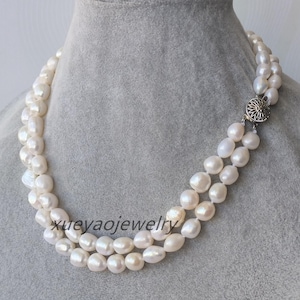 Puede incluir: Un collar de perlas de doble cadena con un cierre plateado. Las perlas son blancas y tienen una forma ligeramente irregular.