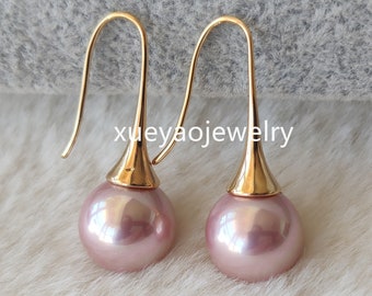 May include: A pair of pink pearl drop earrings with gold hooks. The pearls are round and have a slight iridescent sheen.