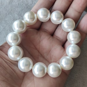 May include: A white pearl bracelet with a total of 10 pearls. The pearls are round and smooth, and they are strung on a clear elastic cord.