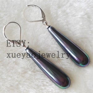 May include: A pair of silver dangle earrings with iridescent black teardrop-shaped stones. The earrings have a hook closure.